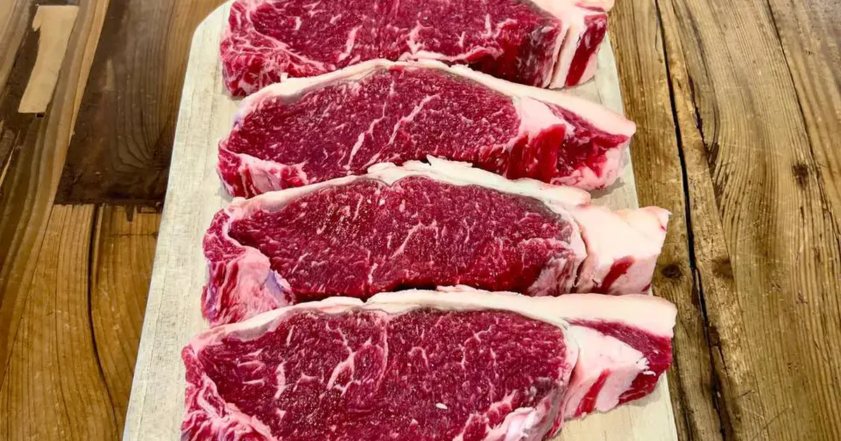 Cuatro porciones de carne de vacuno cruda sobre una tabla de madera
