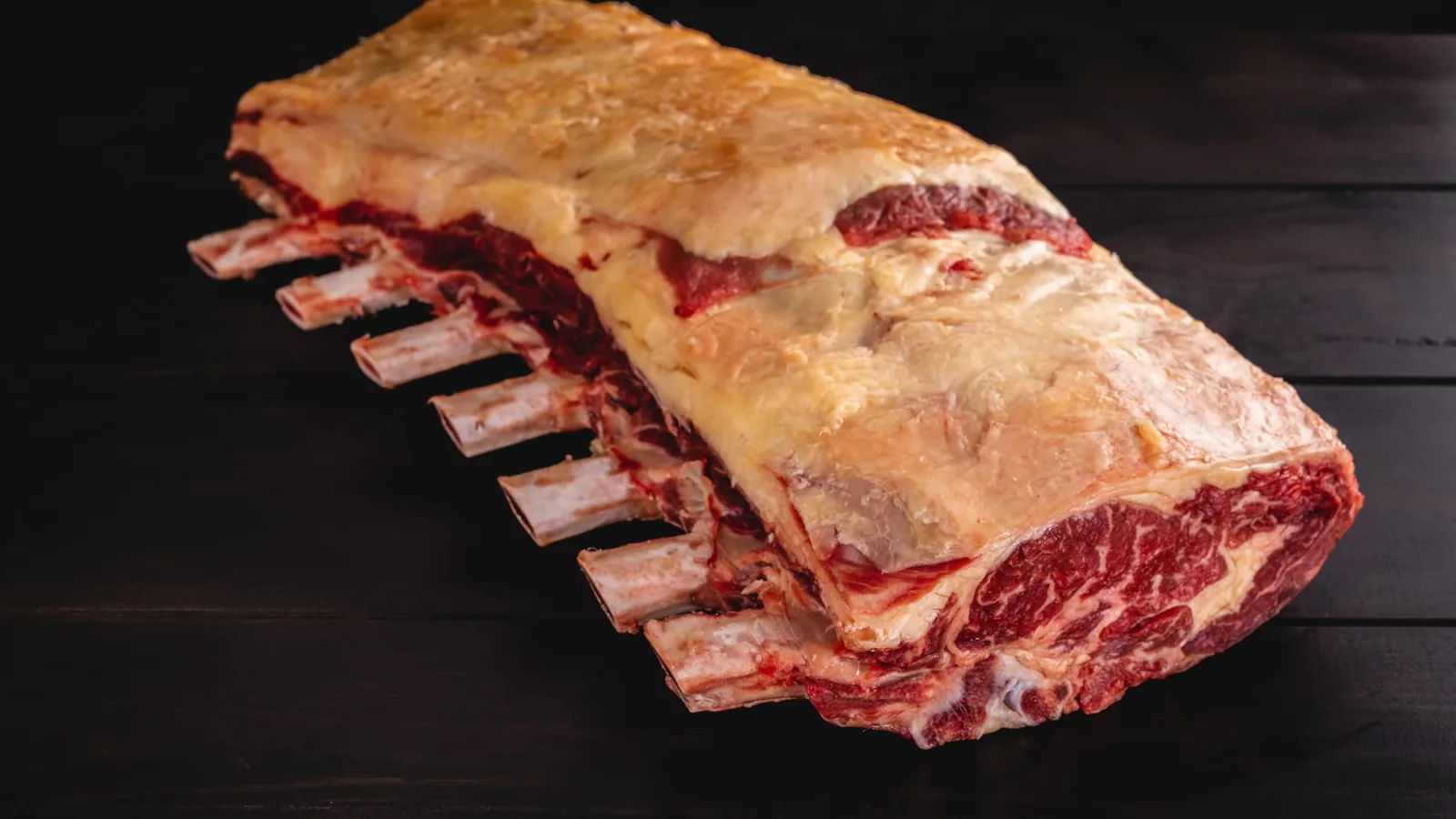 Whole aged beef rib section with external fat and visible bones