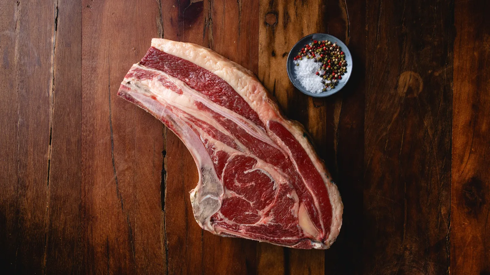 Thick uncooked bone-in rib steak with external fat on wood