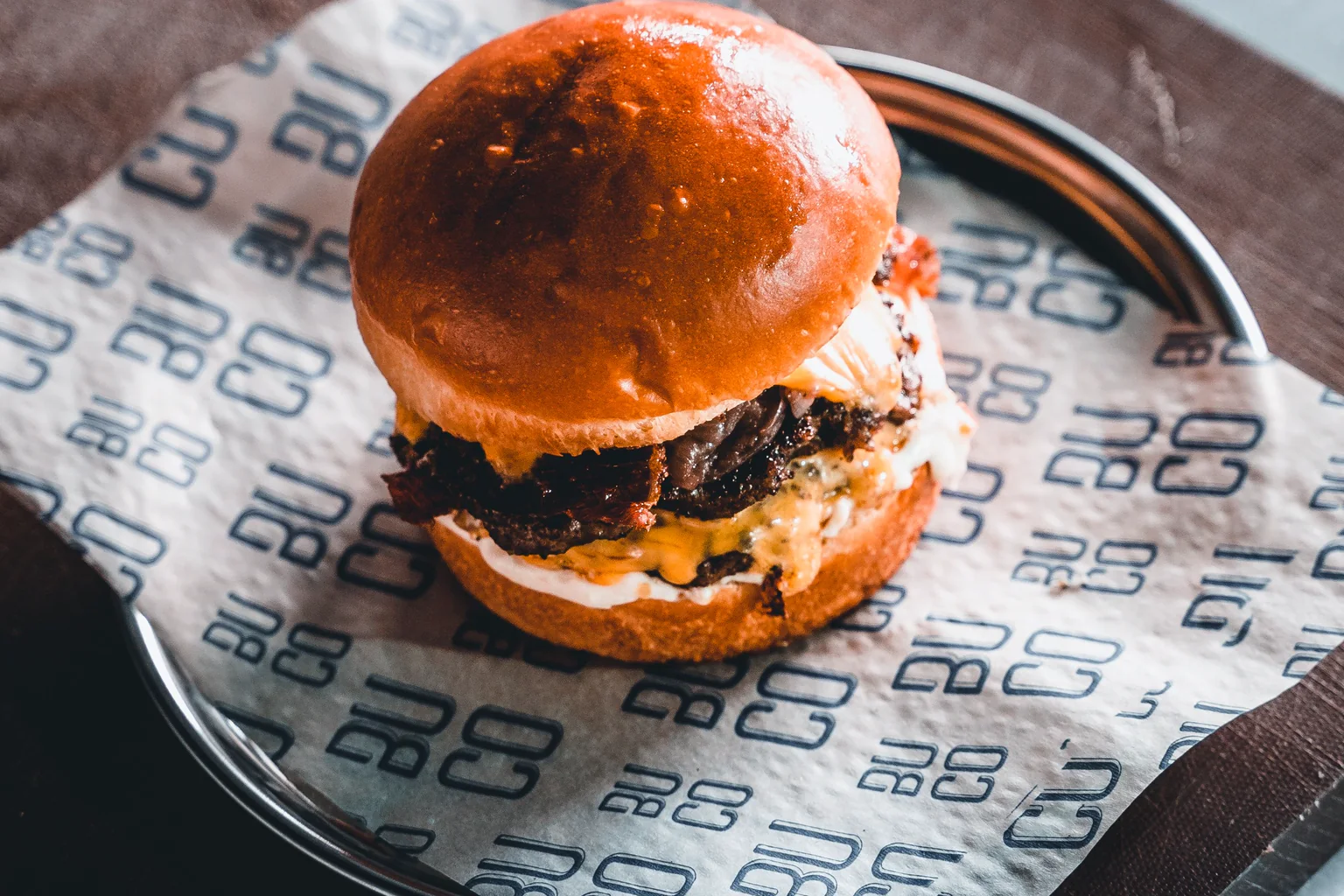Hamburguesa cocinada con queso servida sobre una mesa de madera oscura